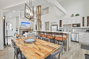 A modern kitchen with white cabinetry, stainless steel appliances, and a wooden dining table with chairs. - Walk to Main Street and Lift | Fireplace (Park City)