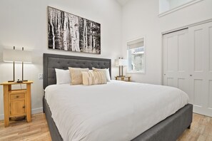 A bedroom with a large bed, two bedside tables, a nightstand, a window with a view, and a door. - Walk to Main Street and Lift | Fireplace (Park City)