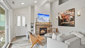 Una sala de estar moderna con chimenea, televisor montado encima y un cuadro abstracto grande en la pared.