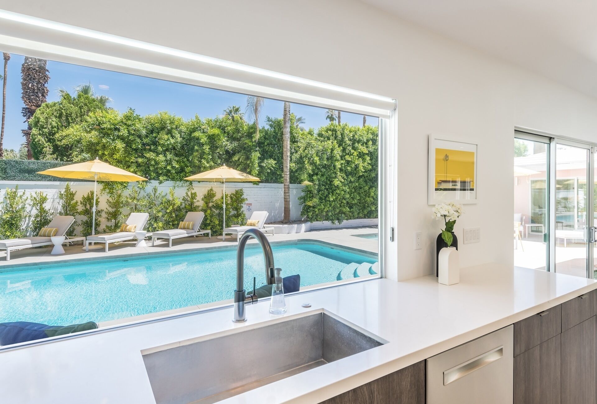 A modern kitchen with a large window overlooking a swimming pool and lush greenery.