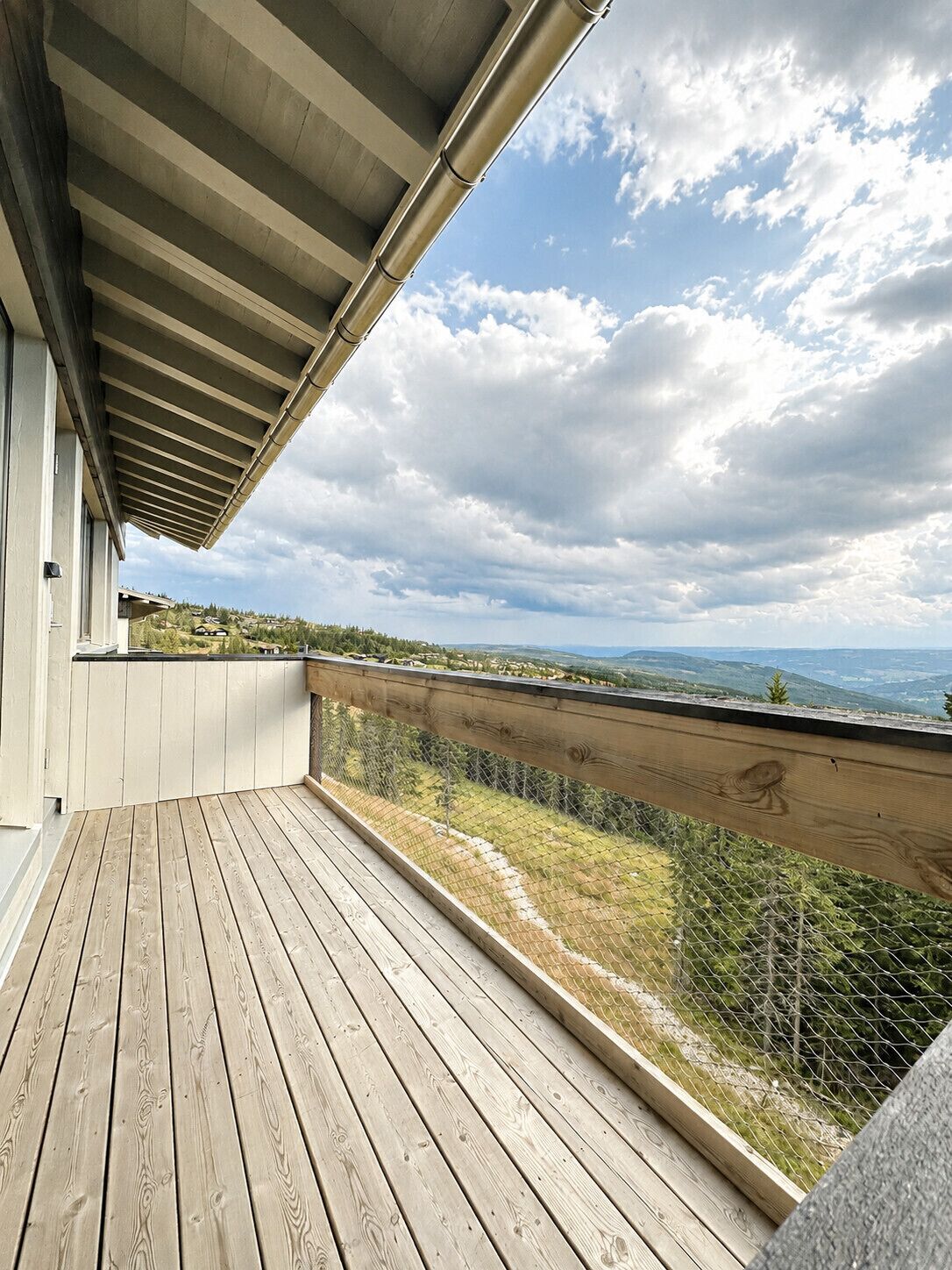 A wooden deck with a metal railing overlooking a hilly landscape.