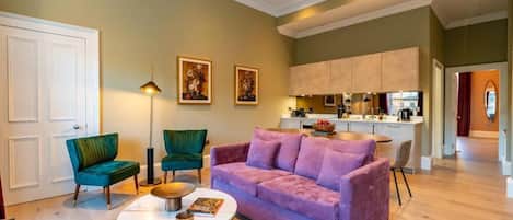 Una sala de estar con un sofá morado, un sillón verde, una mesa de centro y una lámpara de pie.