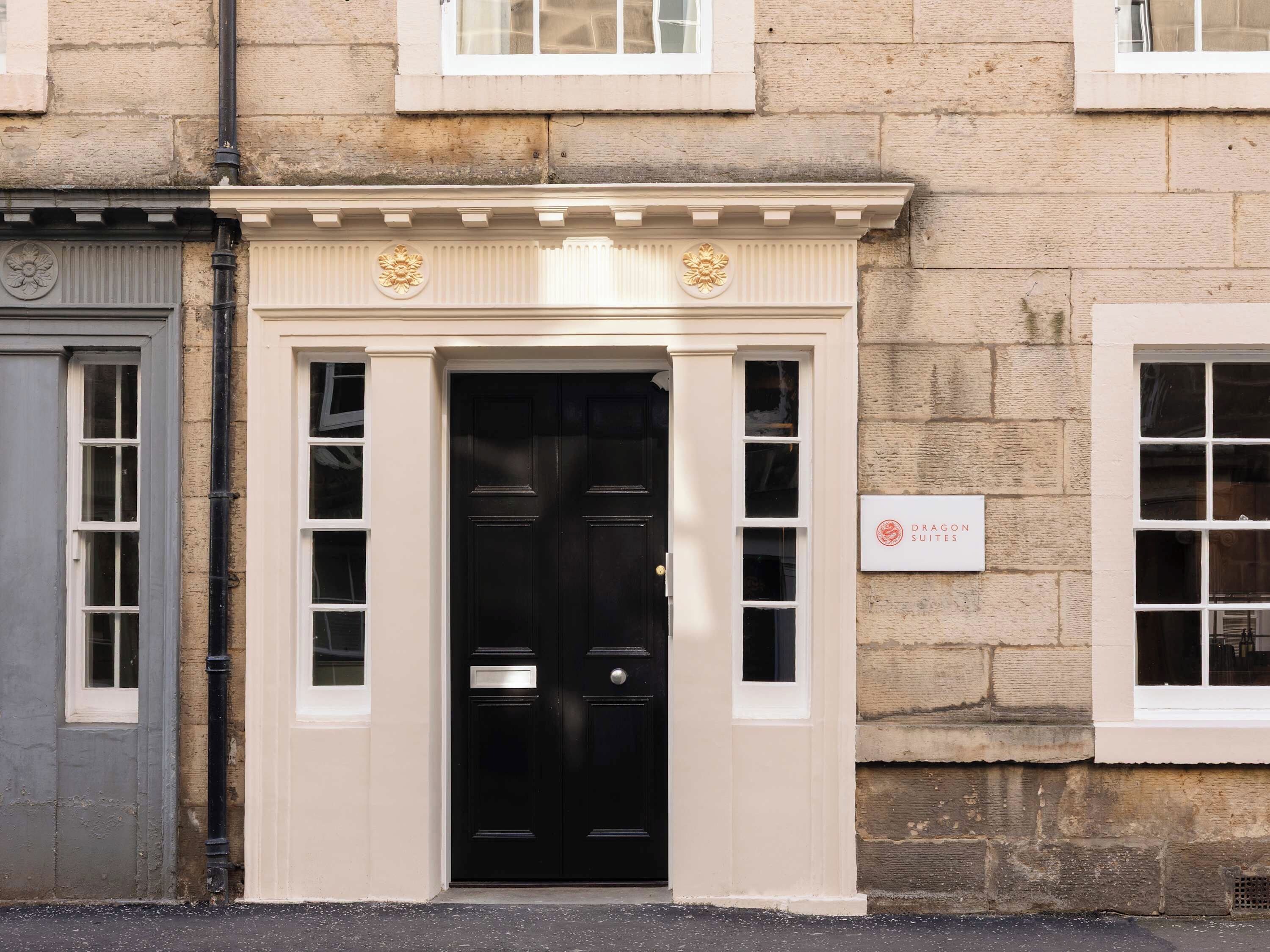 A building facade with a black door, a sign reading 'Dragon Suites,' and a stone wall.