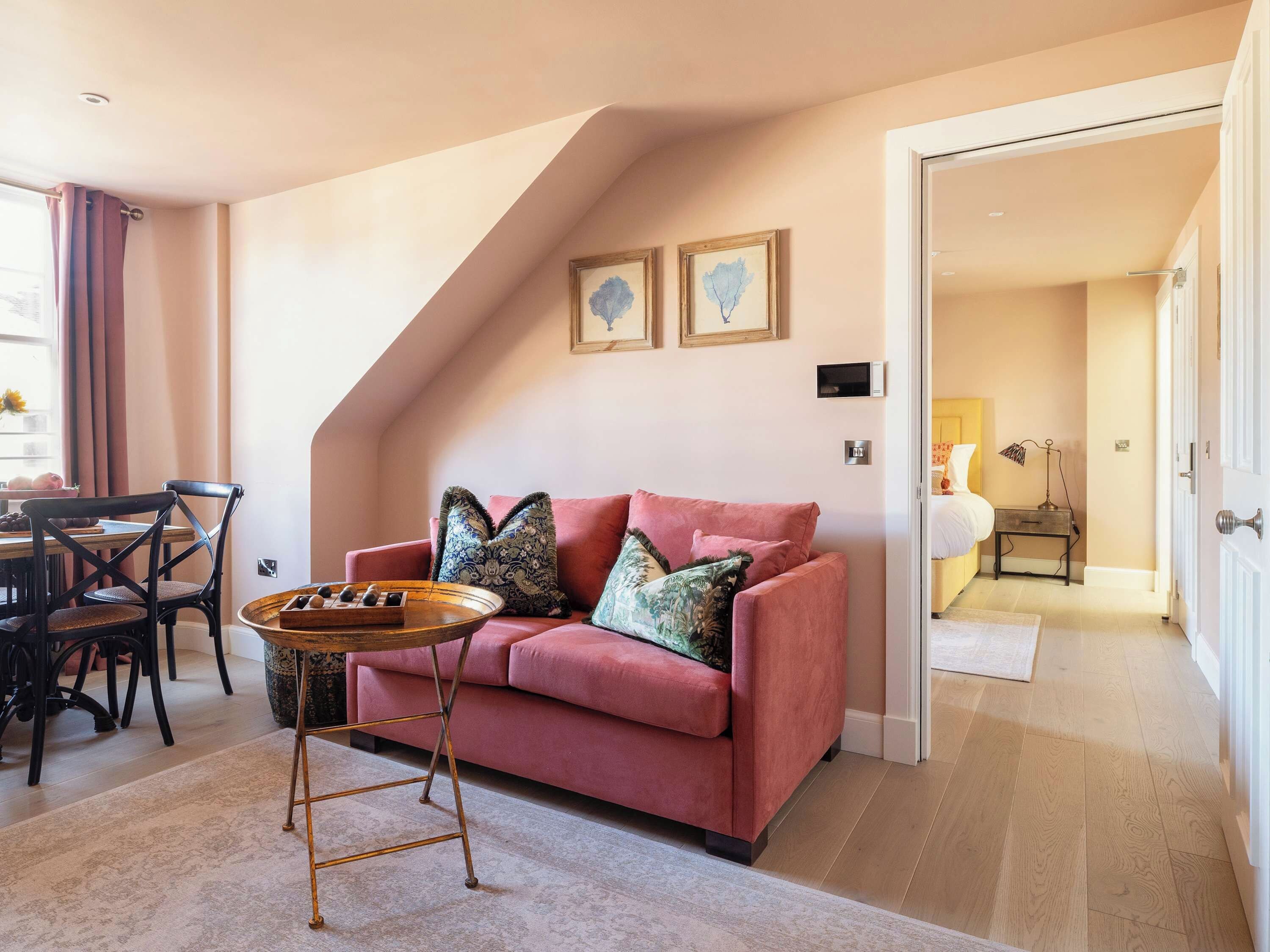 A cozy living room with a pink sofa, a wooden coffee table, and a dining area with a table and chairs.