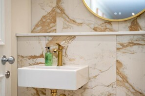 Ein Badezimmer mit einem weißen Waschbecken, einem goldenen Wasserhahn und einer Marmorwand.