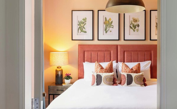 A hotel room with a bed, pillows, a nightstand, a lamp, and framed botanical illustrations on the wall. - Calton Suite - 2 bedroom apartment at Hill Street (Edinburgh)