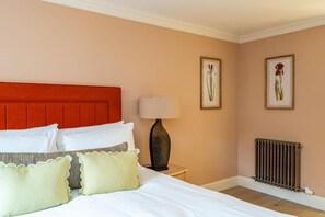 A hotel room with a bed, pillows, a lamp, framed botanical prints, and a radiator. - Pentland Suite - 1 bedroom accessible apartment at Hill Street (Edinburgh)