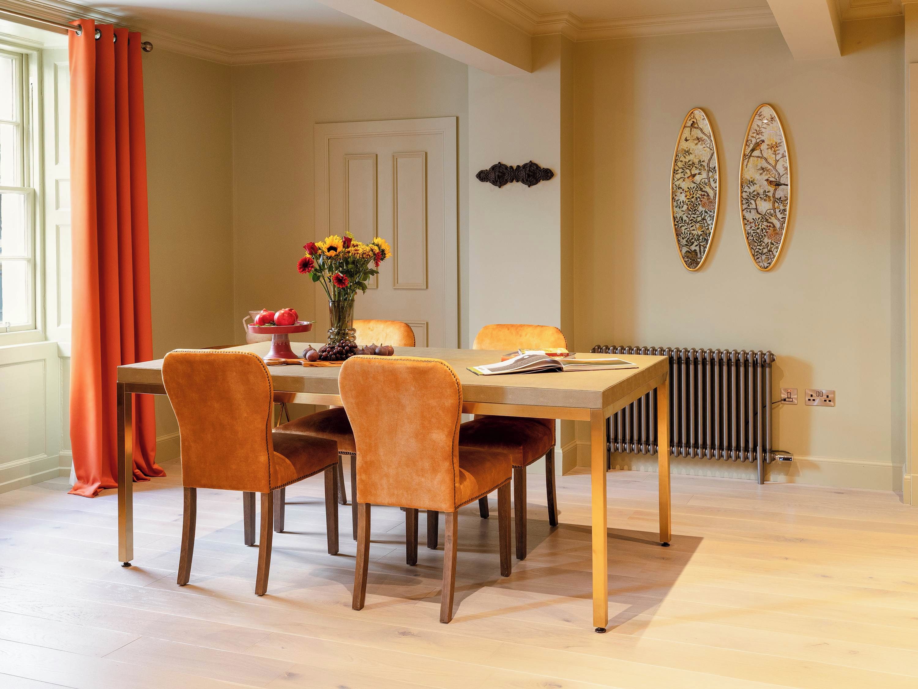 Uma área de jantar com uma mesa posta para quatro pessoas, um vaso com flores e um radiador na parede.