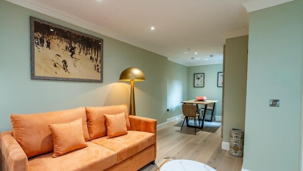 A living room with a sofa, a lamp, a dining area with a table and chairs, and a framed picture on the wall. - Pentland Suite - 1 bedroom accessible apartment at Hill Street (Edinburgh)