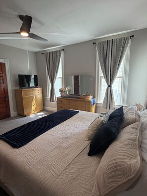 A bedroom with a bed, dresser, vanity, and a ceiling fan.
