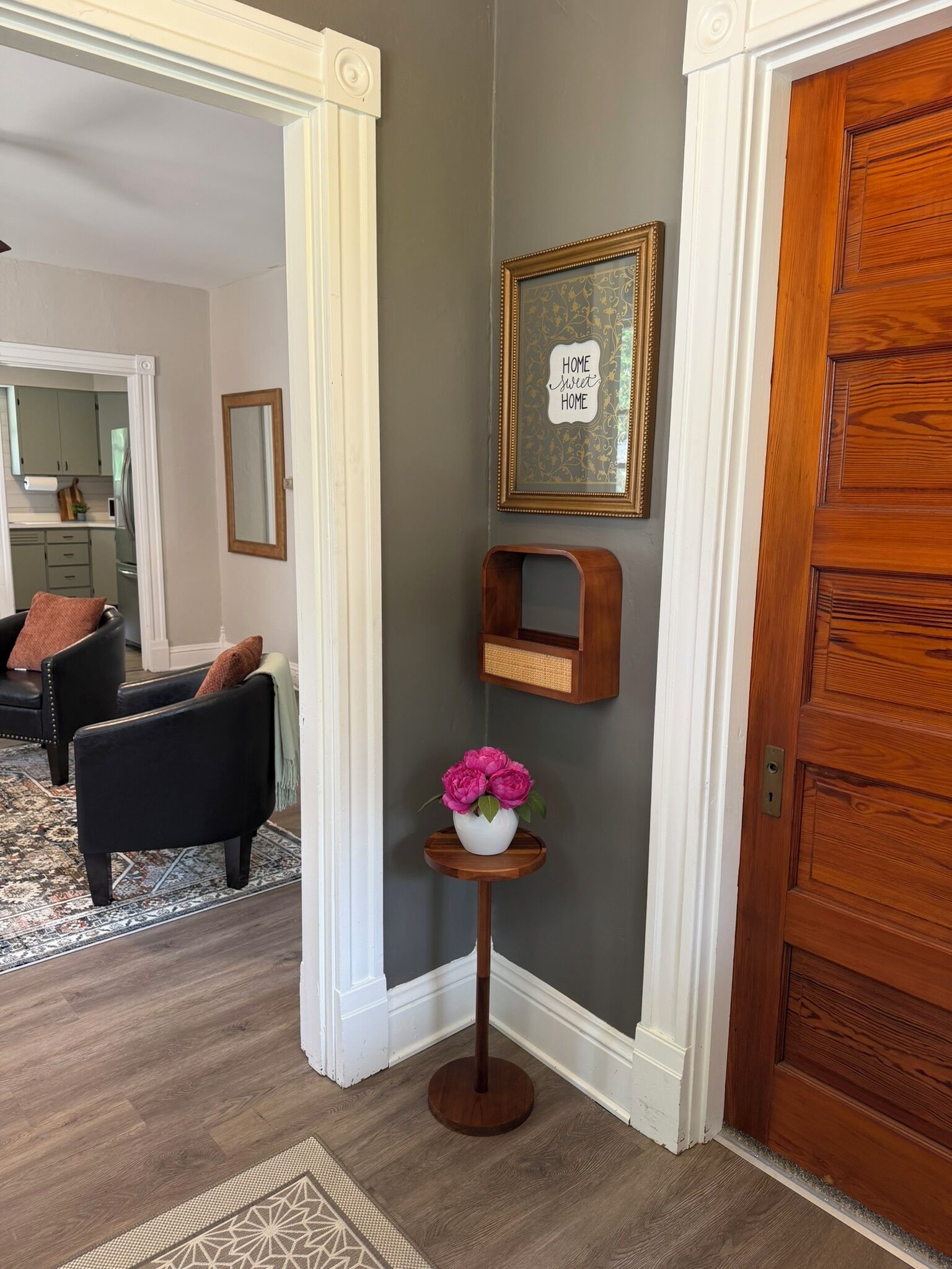 A hallway with a wooden door, a framed sign, a small wooden shelf, and a vase with flowers.