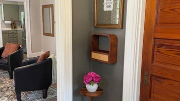 A hallway with a wooden door, a framed sign, a small wooden shelf, and a vase with flowers.