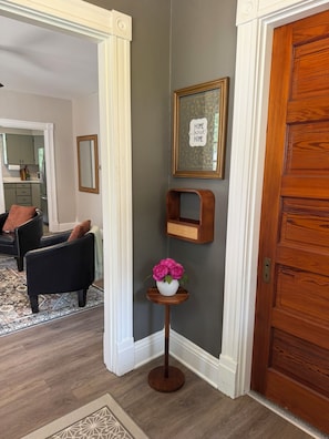 A hallway with a wooden door, a framed sign, a small wooden shelf, and a vase with flowers.