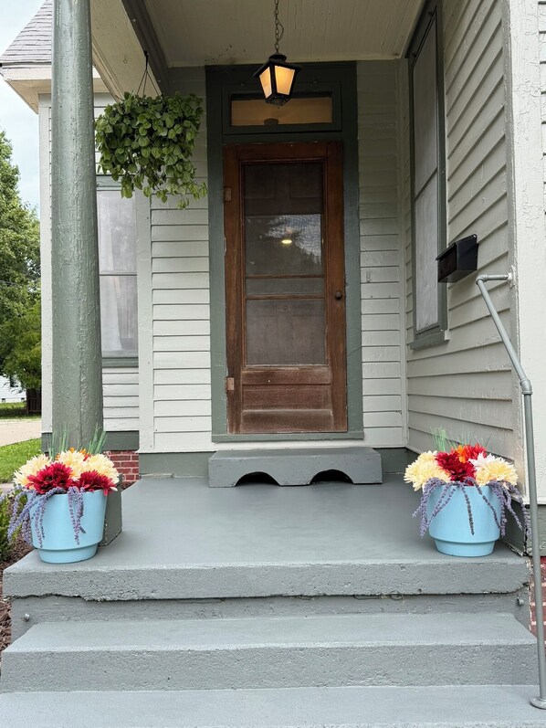A house with a front porch, a wooden door, and two flower pots with flowers.