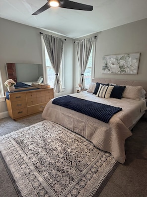 A bedroom with a bed, a dresser, a rug, and a ceiling fan.