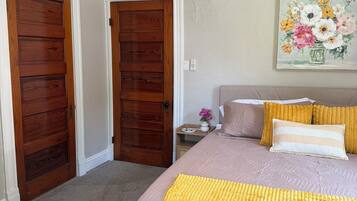 Une chambre à coucher avec un lit, deux portes en bois, une table de chevet, un tableau et un ventilateur de plafond.