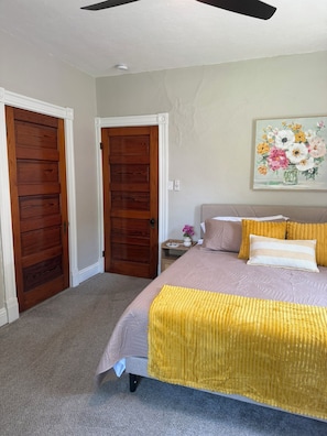 A bedroom with a bed, two wooden doors, a nightstand, a painting, and a ceiling fan.