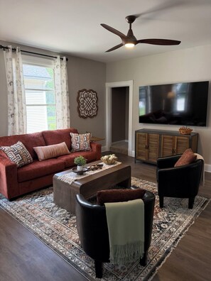 A living room with a sofa, armchairs, a coffee table, a TV, and a ceiling fan.