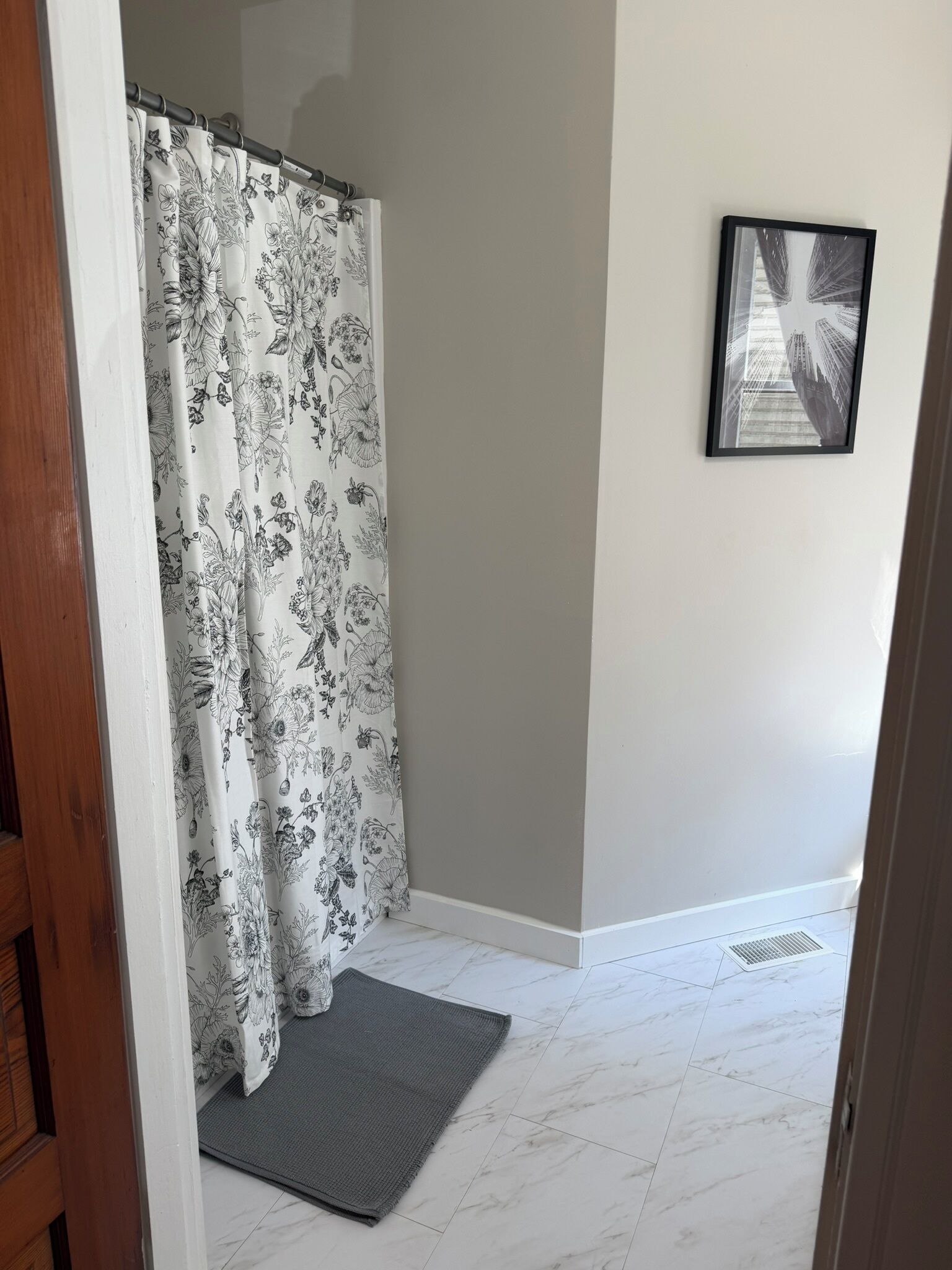A bathroom with a shower curtain, a framed picture on the wall, and a tiled floor.