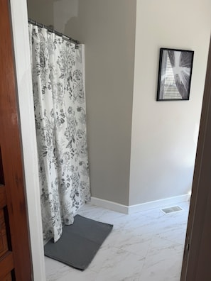 A bathroom with a shower curtain, a framed picture on the wall, and a tiled floor.