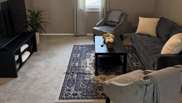 Un salon confortable avec un téléviseur à écran plat, un canapé, une table basse et un tapis à motifs.