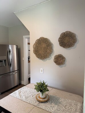 A kitchen with a stainless steel refrigerator, a potted plant on a round wooden table, and three wall-mounted decorative items.