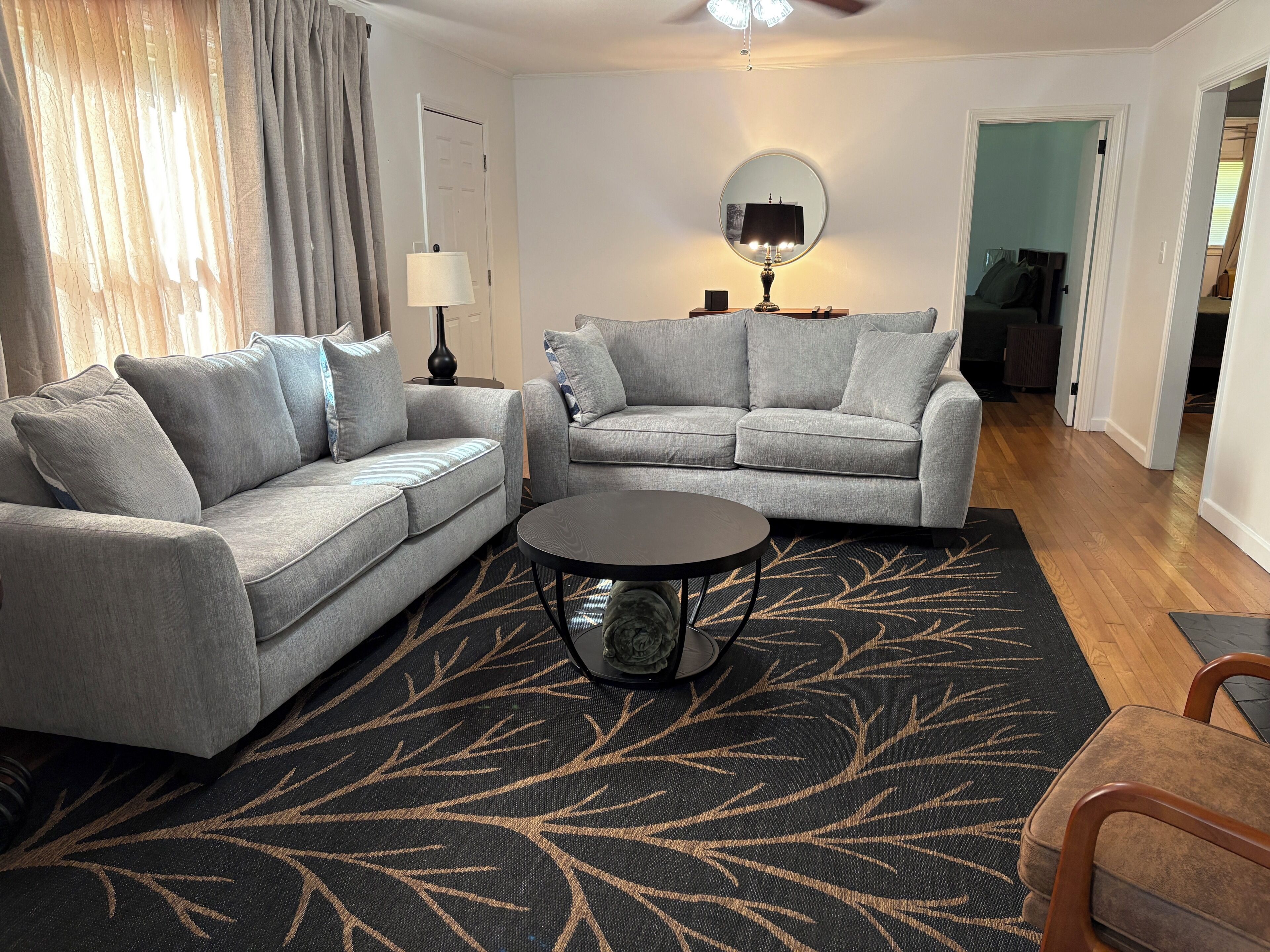 A living room with two grey sofas, a round coffee table, a black rug with a leaf pattern, a lamp, and a mirror on the wall.
