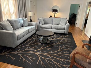 Een woonkamer met twee grijze banken, een ronde salontafel en een vloerkleed met patroon.