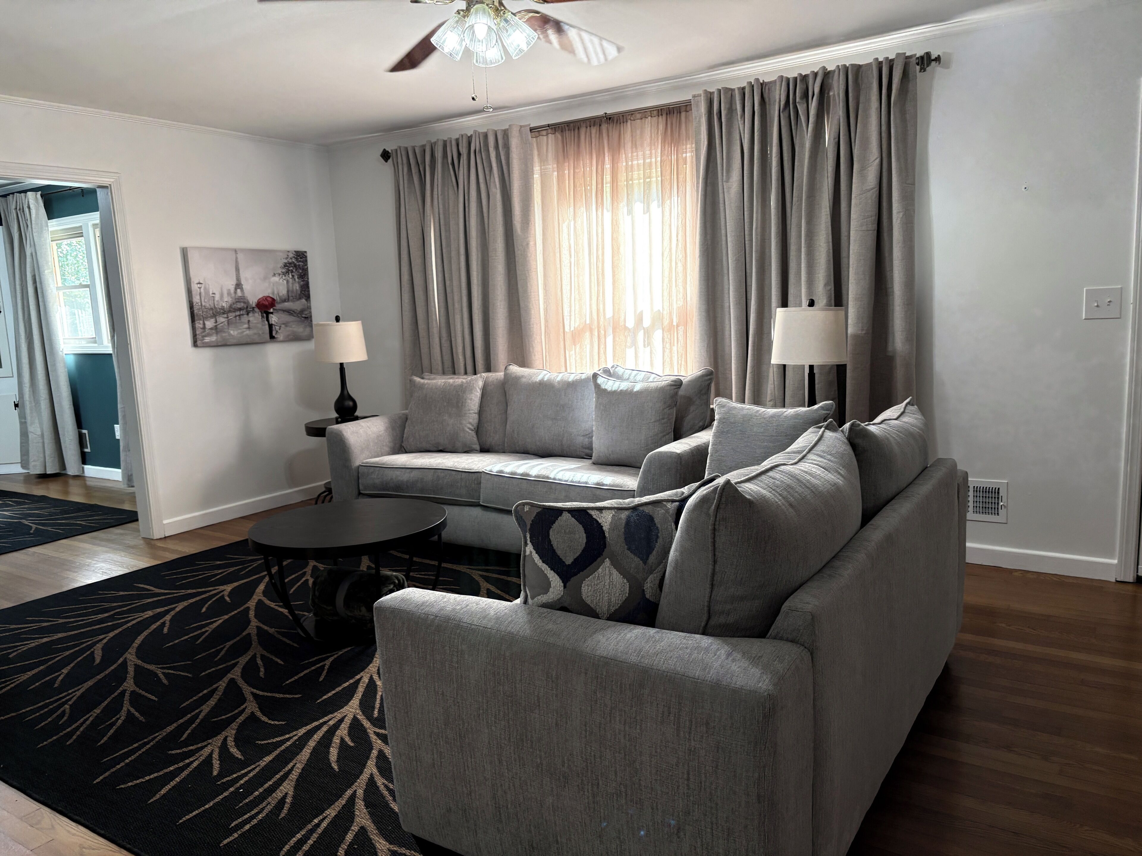 A living room with a grey sofa, two side tables with lamps, a patterned rug, and a ceiling fan.