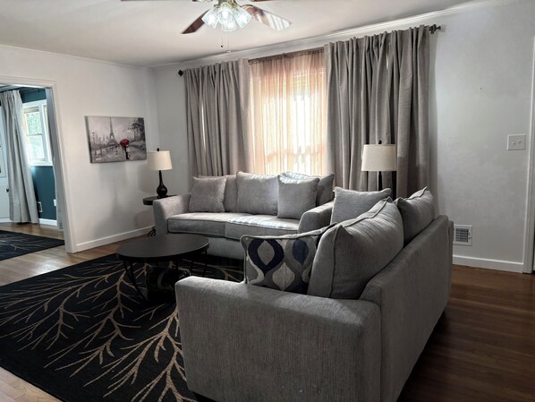 A living room with a grey sofa, two side tables with lamps, a patterned rug, and a ceiling fan.