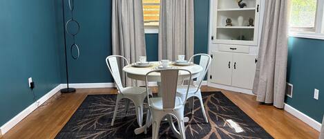 Un coin repas avec une table ronde, des chaises blanches, un tapis à motifs et un buffet blanc aux portes vitrées.