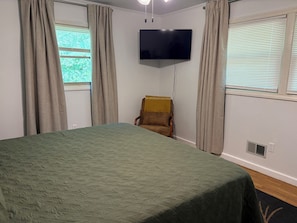 Quarto com cama, televisão na parede e uma cadeira.