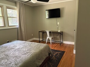 Een slaapkamer met een bed, bureau, stoel, televisie en raam.