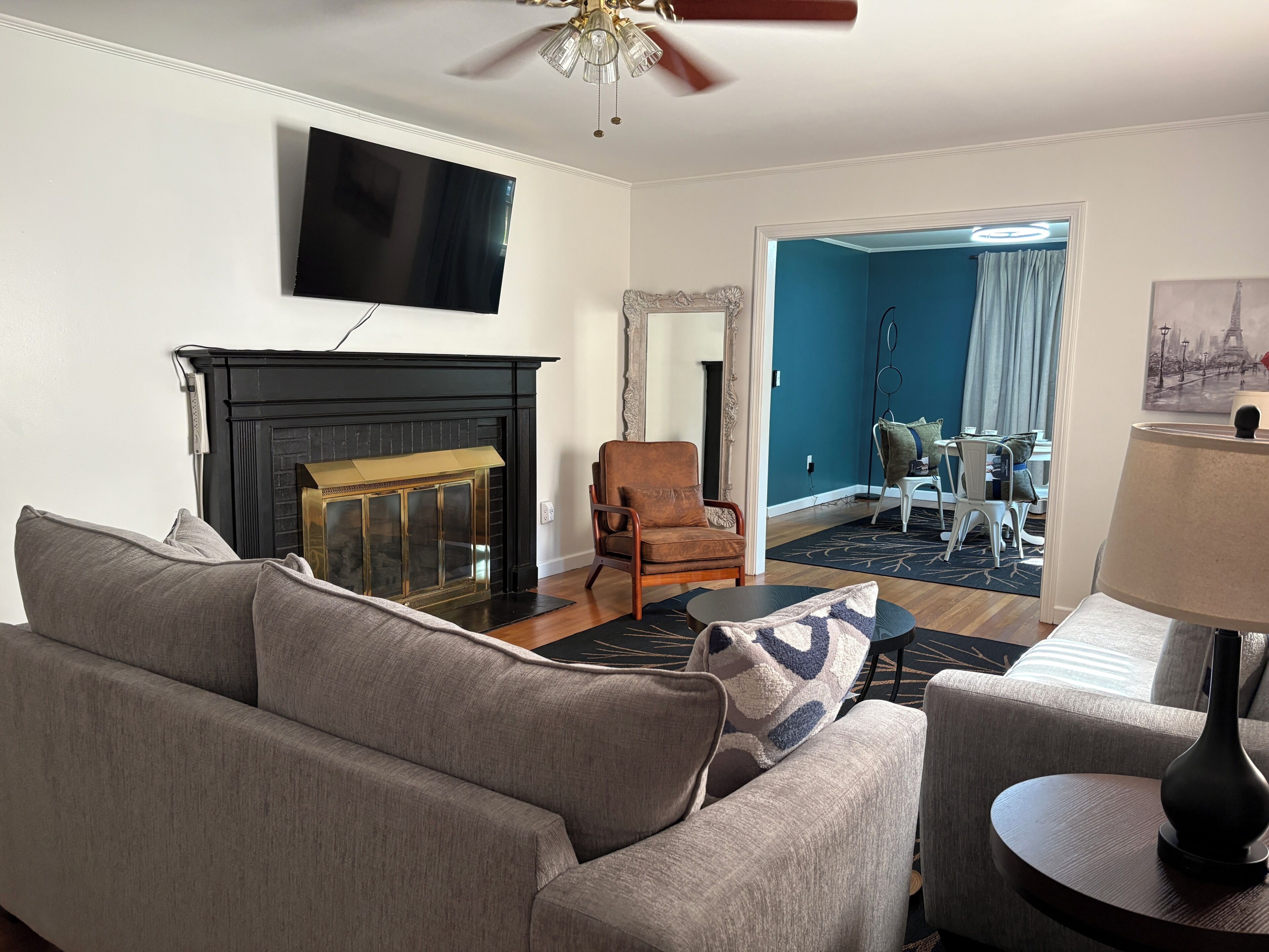 A living room with a fireplace, a television mounted on the wall, a ceiling fan, and a view into another room with a dining area.