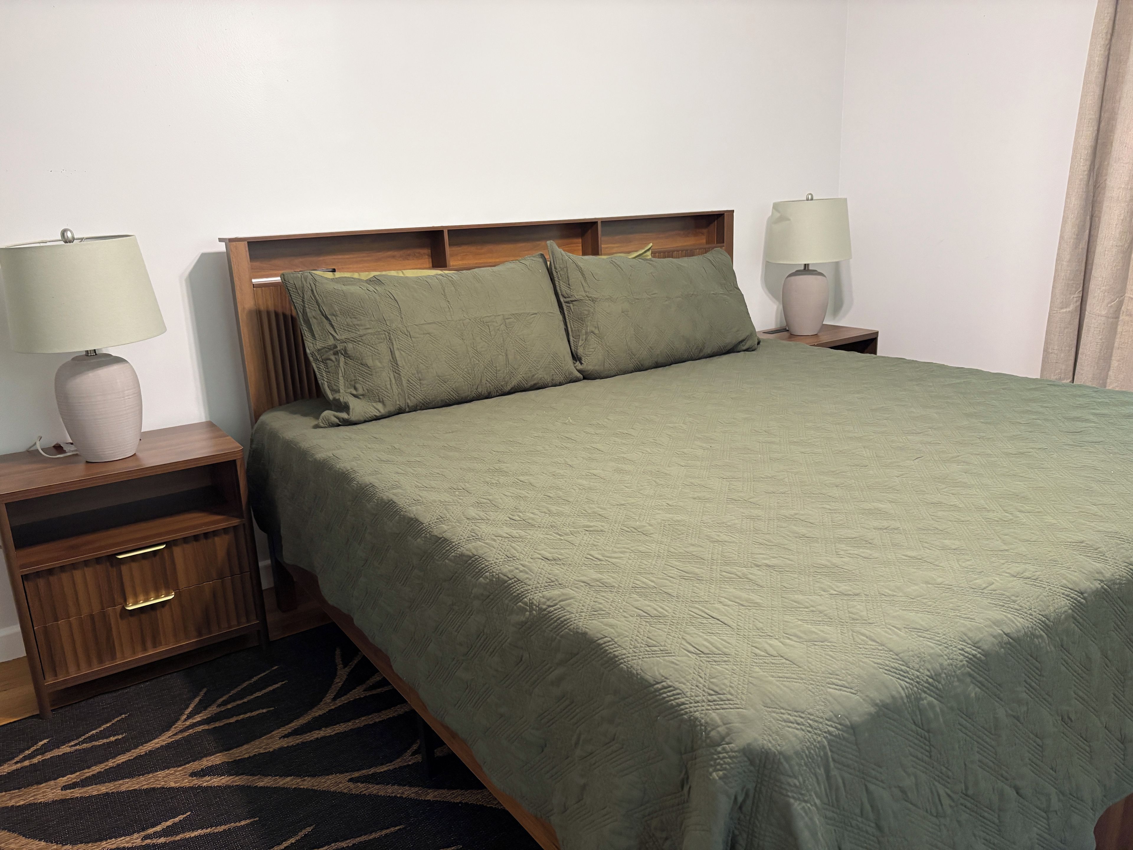 Una habitación de hotel con una cama, dos mesitas de noche, lámparas, un tocador y una alfombra estampada.
