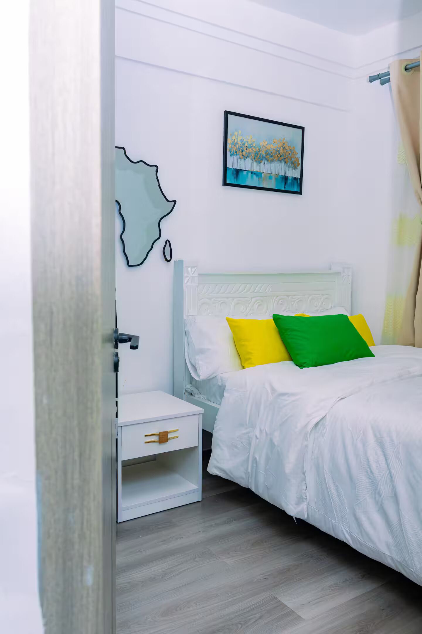 Un dormitorio con cama, mesita de noche, un cuadro colgado en la pared y una puerta.