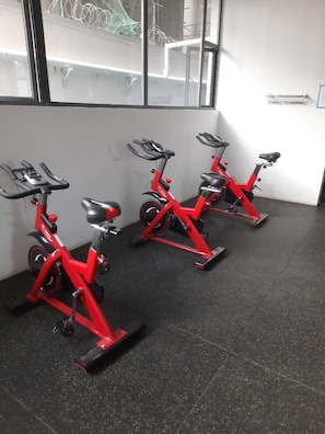 Three stationary bikes in a room with a black floor and a window with a view of a building outside. - Apartment in Kilimani, Nairobi, Kenya (Nairobi)