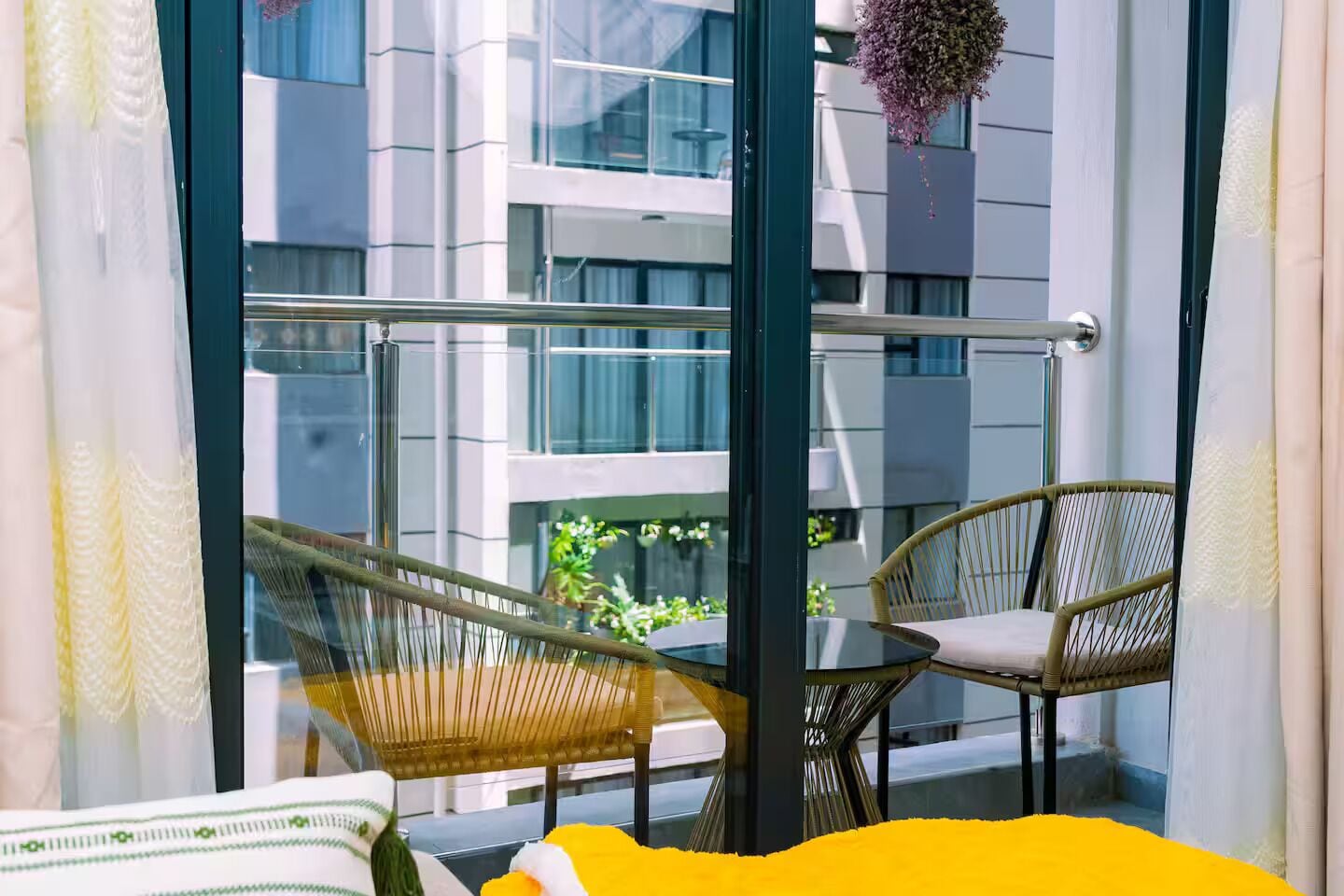 A balcony with wicker furniture, a glass balustrade, and a view of a modern building.