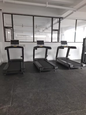 Drei Laufbänder in einem Raum mit großen Fenstern und einem sichtbaren Bereich mit Fitnessgeräten.