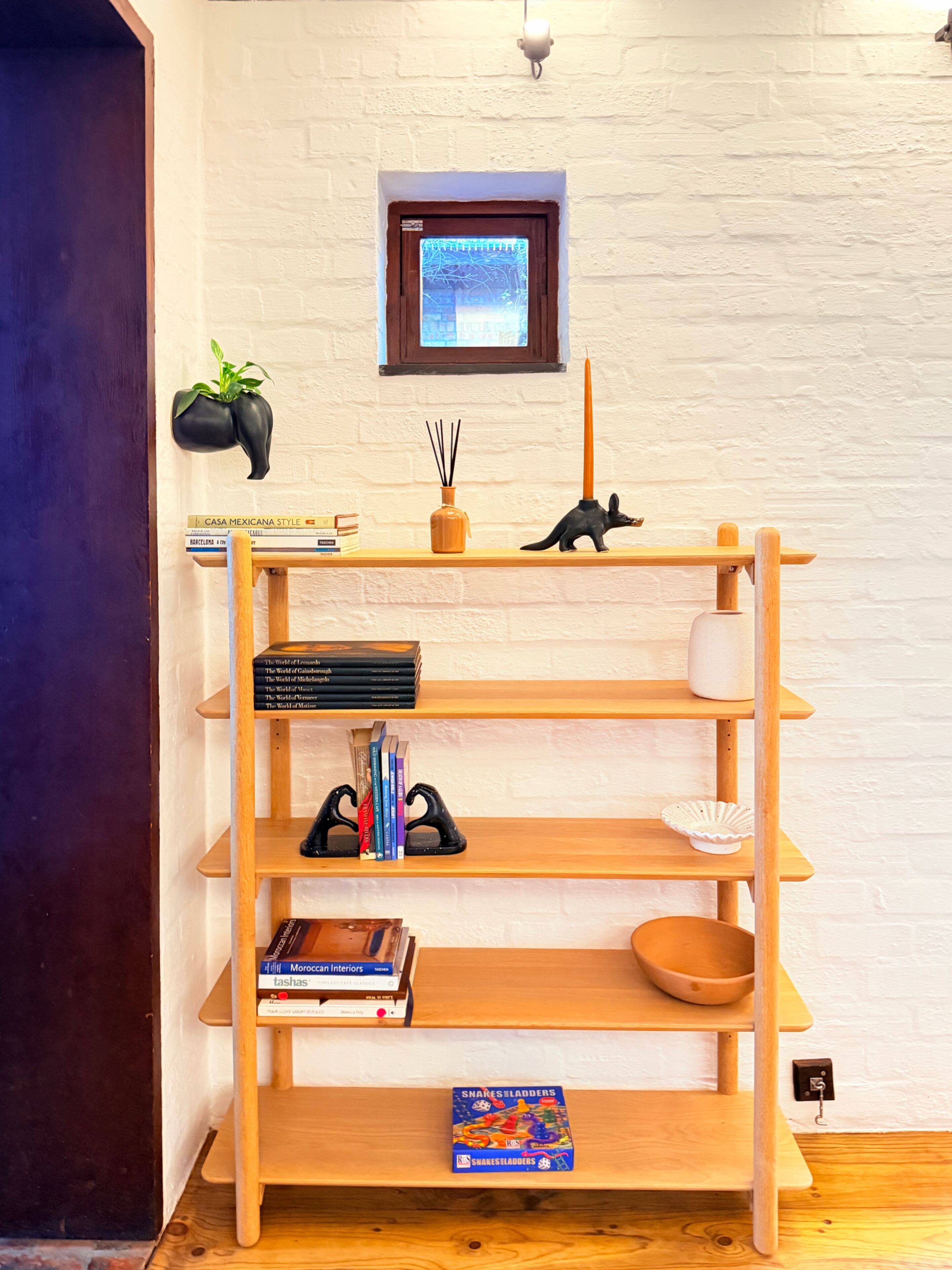 Une bibliothèque en bois remplie de livres, une petite plante en pot et quelques objets décoratifs, le tout placé devant un mur de briques blanches.