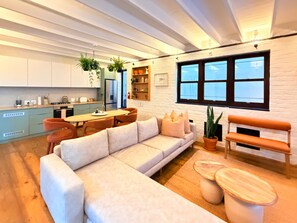 A modern kitchen with white cabinets, a dining table, and chairs. There is a sofa and a bench in the living area. - Curated sanctuary in the heart of the city (Cape Town)