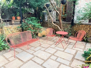 A patio with red metal chairs and a small round table, surrounded by stone tiles and greenery. - Curated sanctuary in the heart of the city (Cape Town)