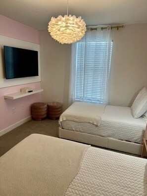 Quarto com duas camas, televisão, luminária decorativa e janela com persianas.