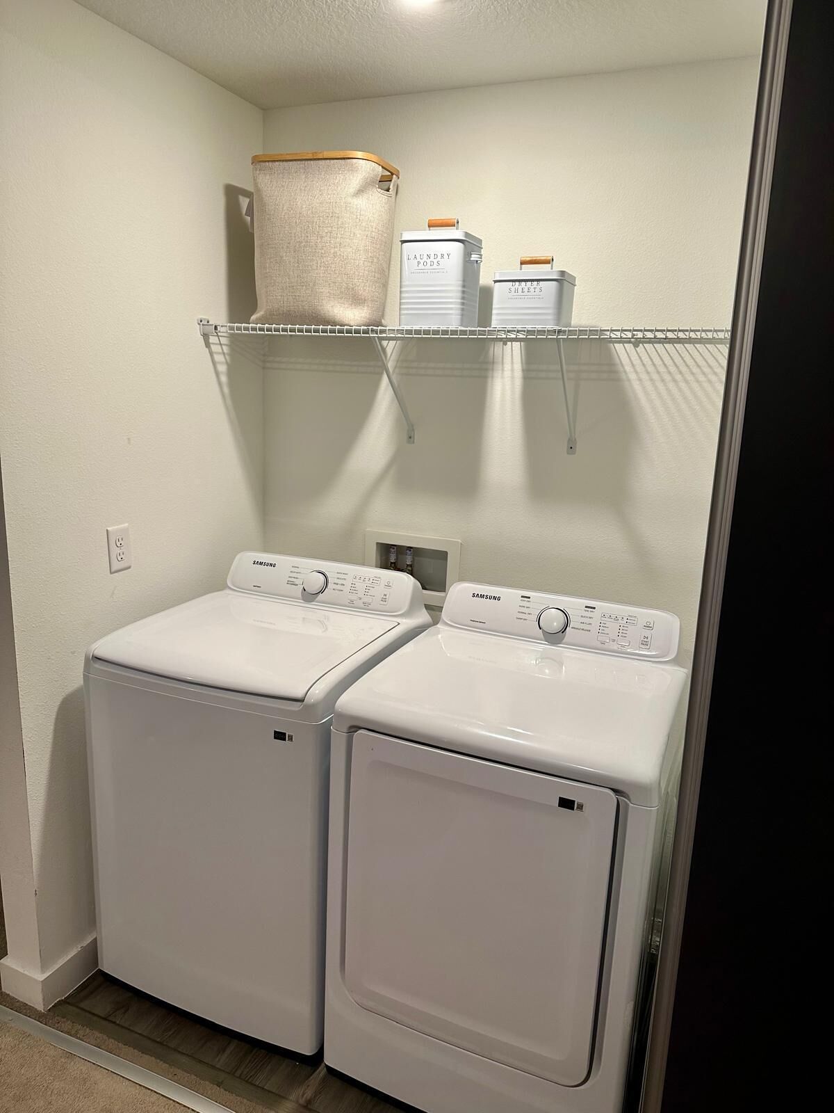 A laundry room with two white Samsung washing machines and storage shelves above them.