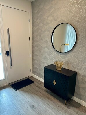 A hallway with a white door, a dark blue cabinet with a gold vase, and a round mirror on the wall. - Magical Family Escape! Spacious 3BR Home Minutes from Disney! (Kissimmee)