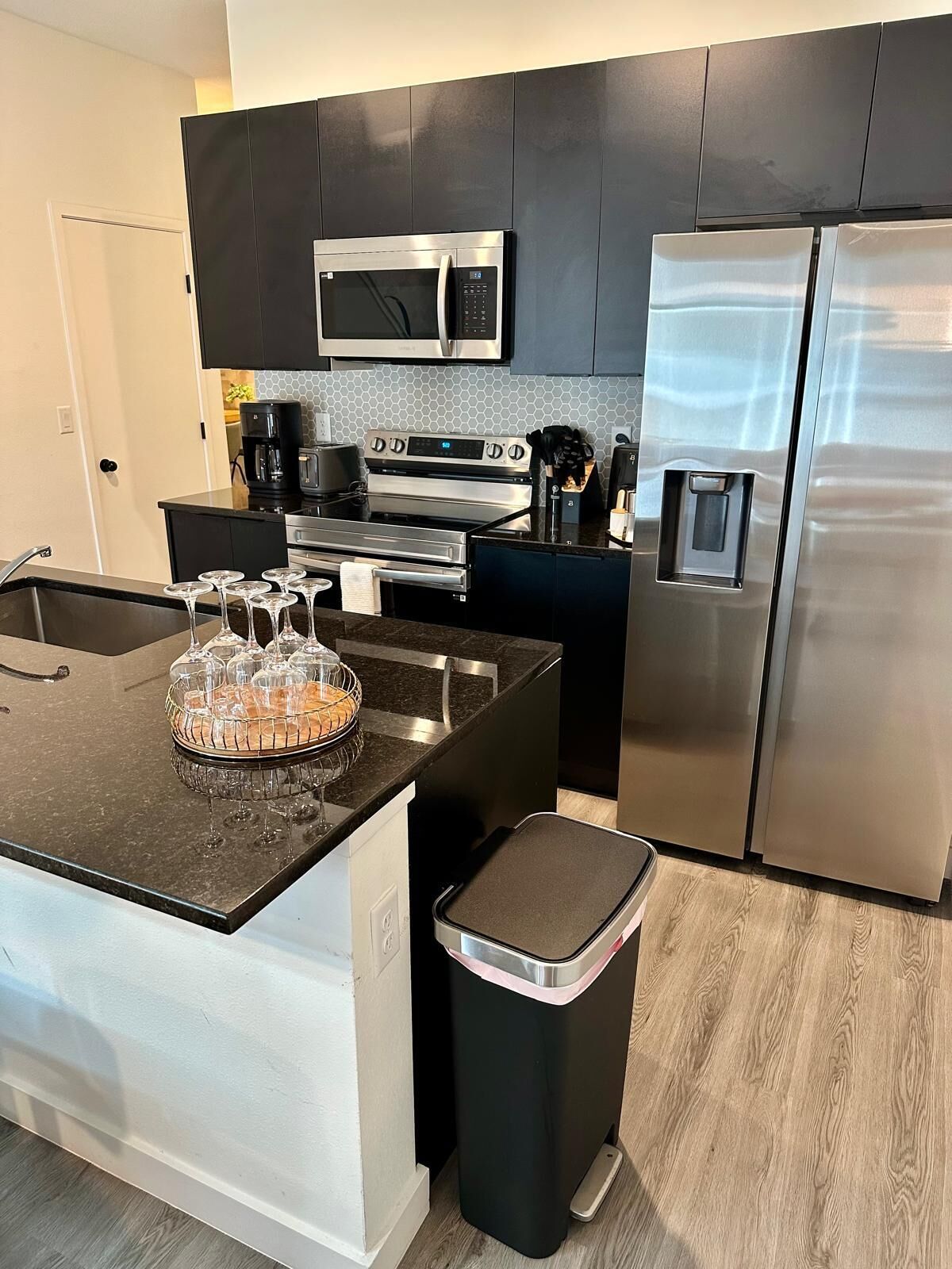 A modern kitchen with a central island, stainless steel appliances, and a black trash bin.