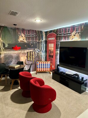 Quarto com televisão de tela plana, um telefone público vermelho, um jogo de tabuleiro e uma estante de livros.