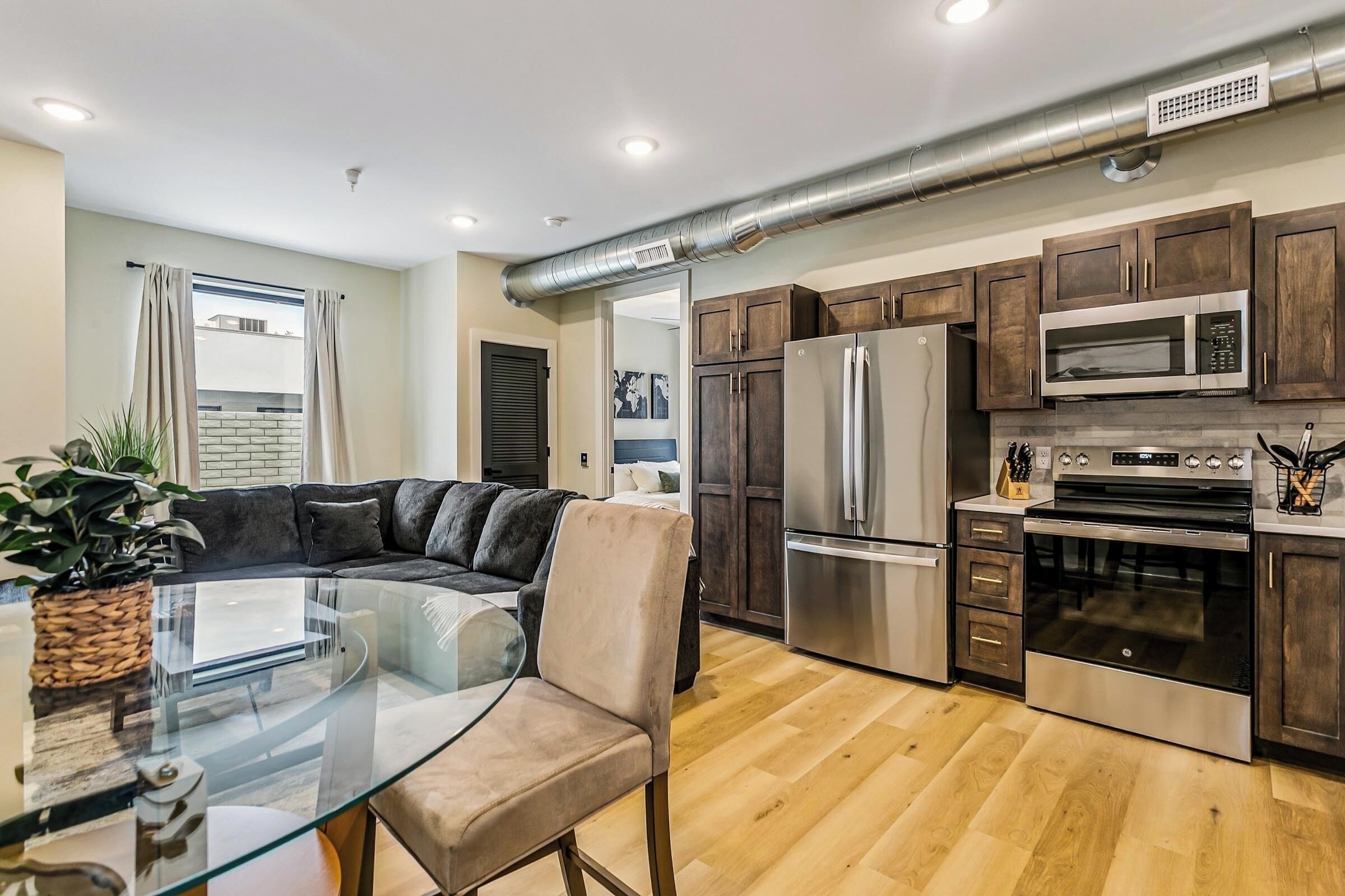 A modern kitchen with stainless steel appliances, wooden cabinets, and a glass dining table.