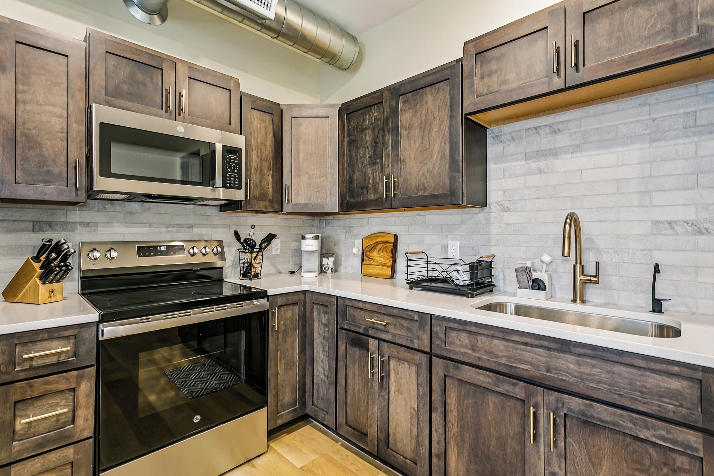 A modern kitchen with dark wood cabinets, stainless steel appliances, and a white countertop.