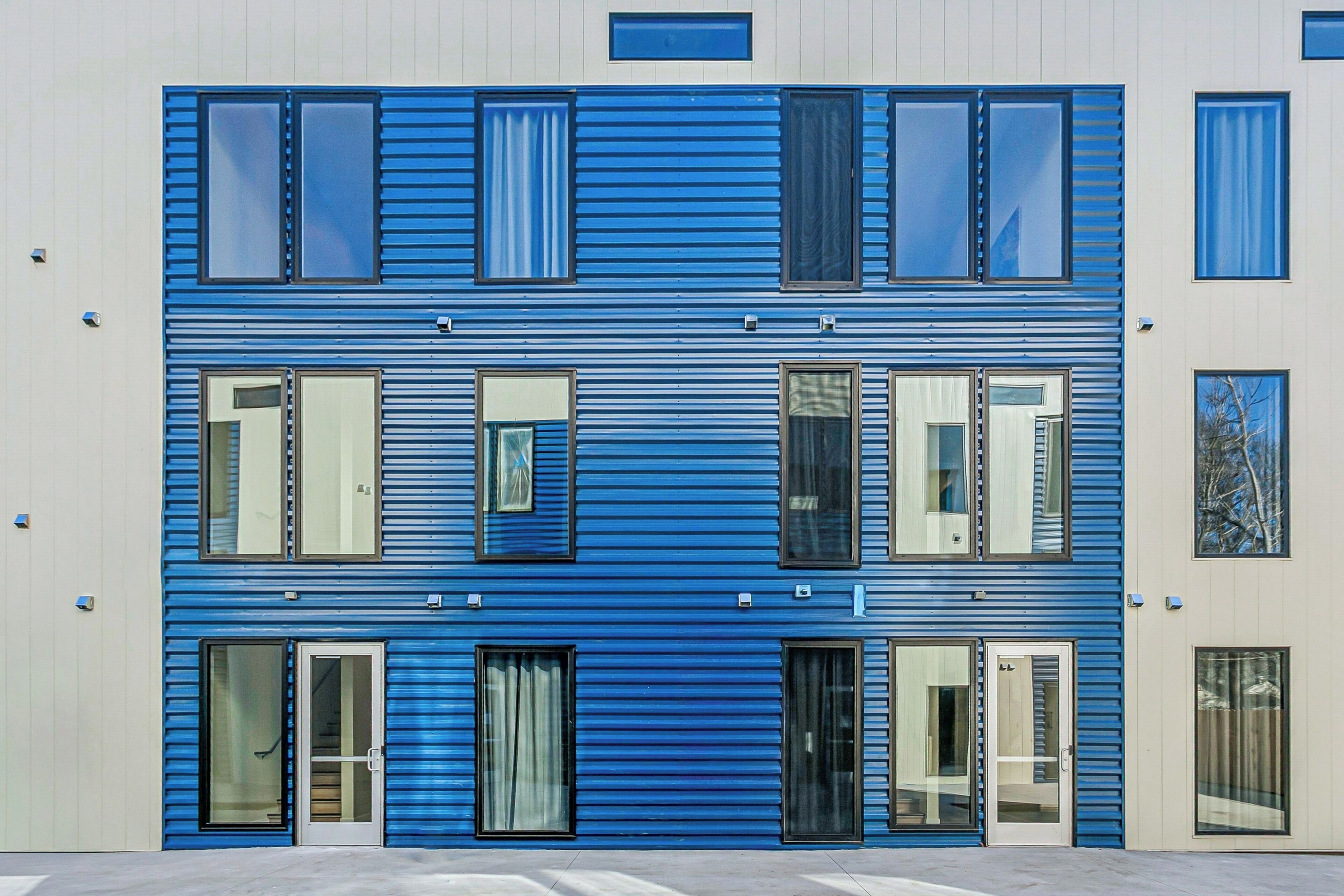 Een modern gebouw met een blauwe gevel, meerdere ramen en deuren.